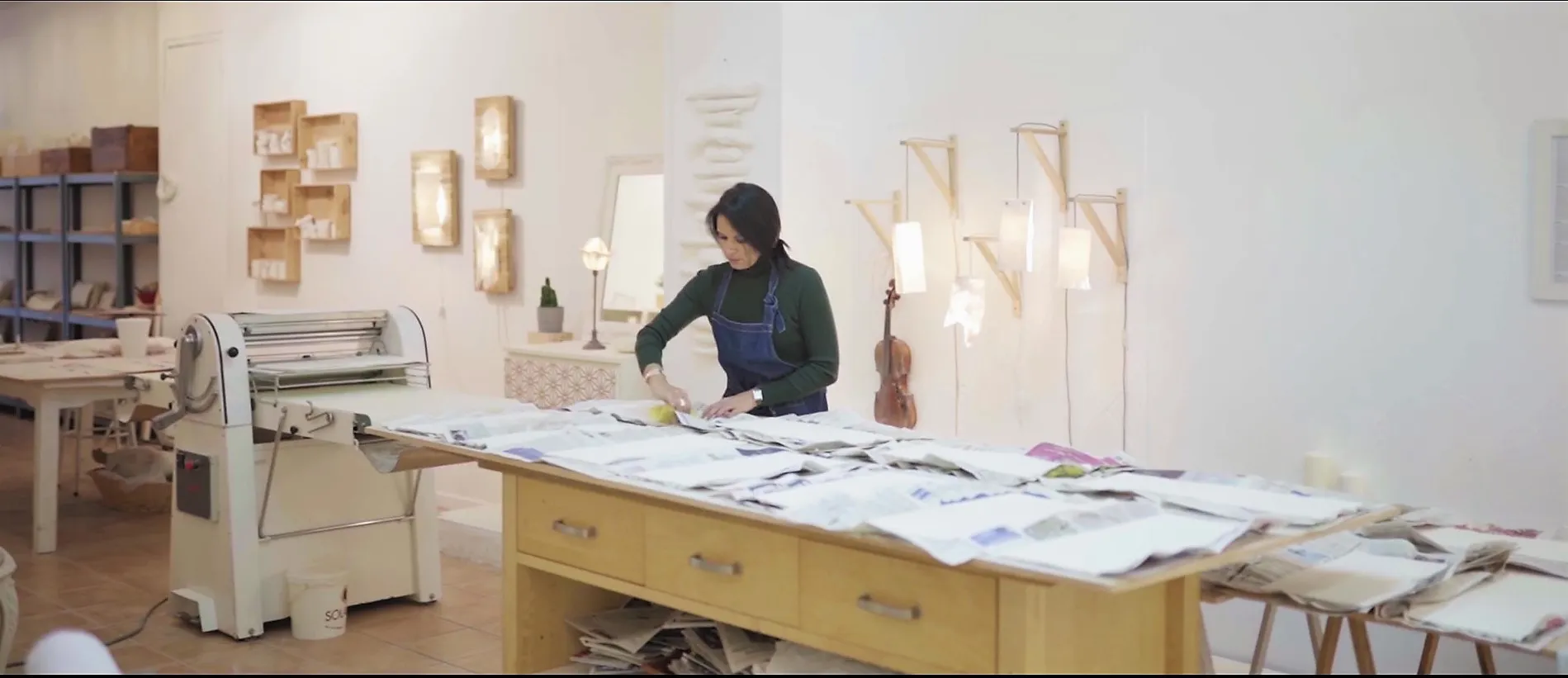 Stéphanie Titus à sa table de travail dans l’atelier de Jacou, entourée de plaques de porcelaine et de pièces lumineuses.