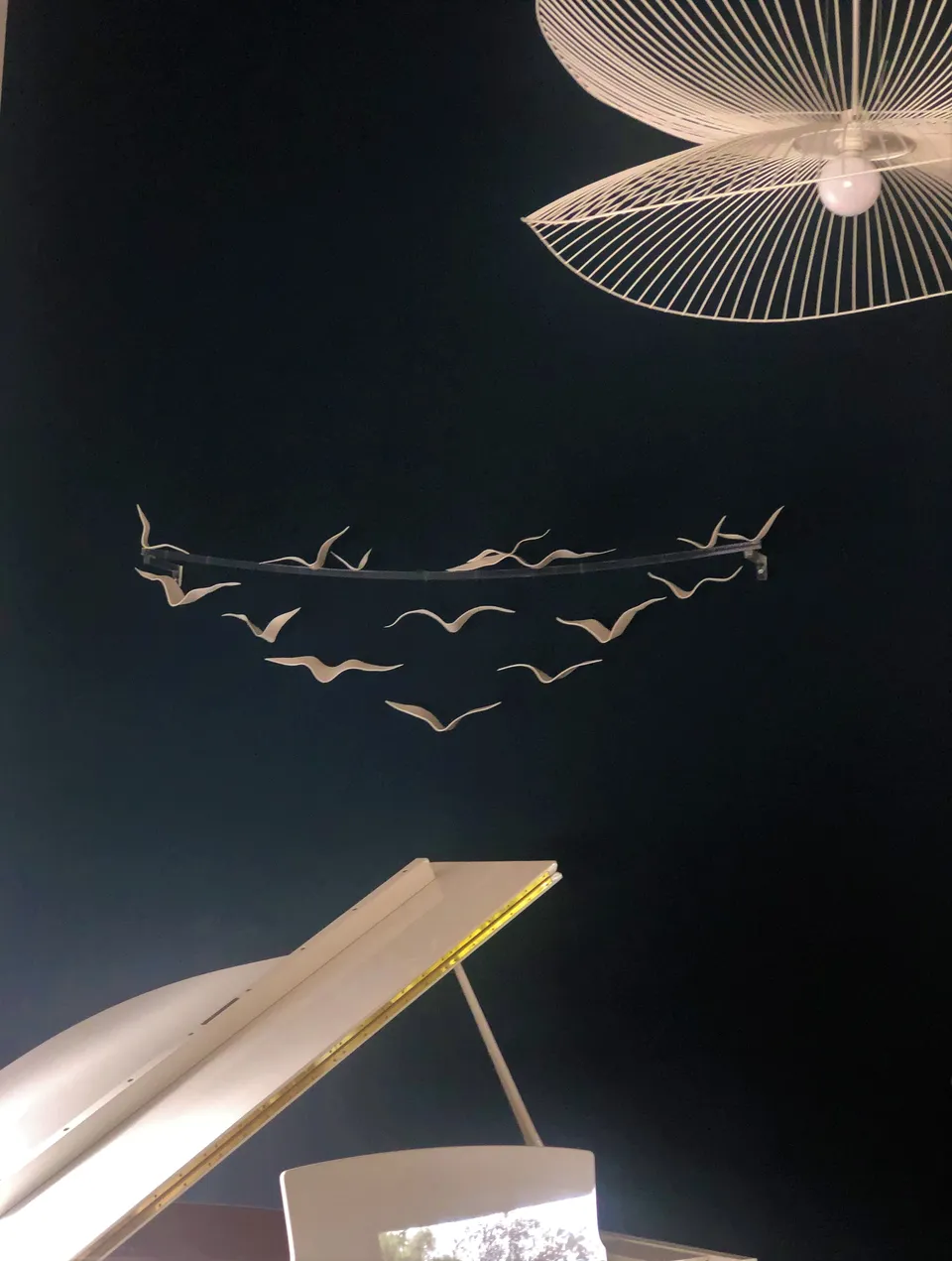 Birds, vol d’oiseaux de porcelaine fixé sur un arc devant un mur bleu nuit.