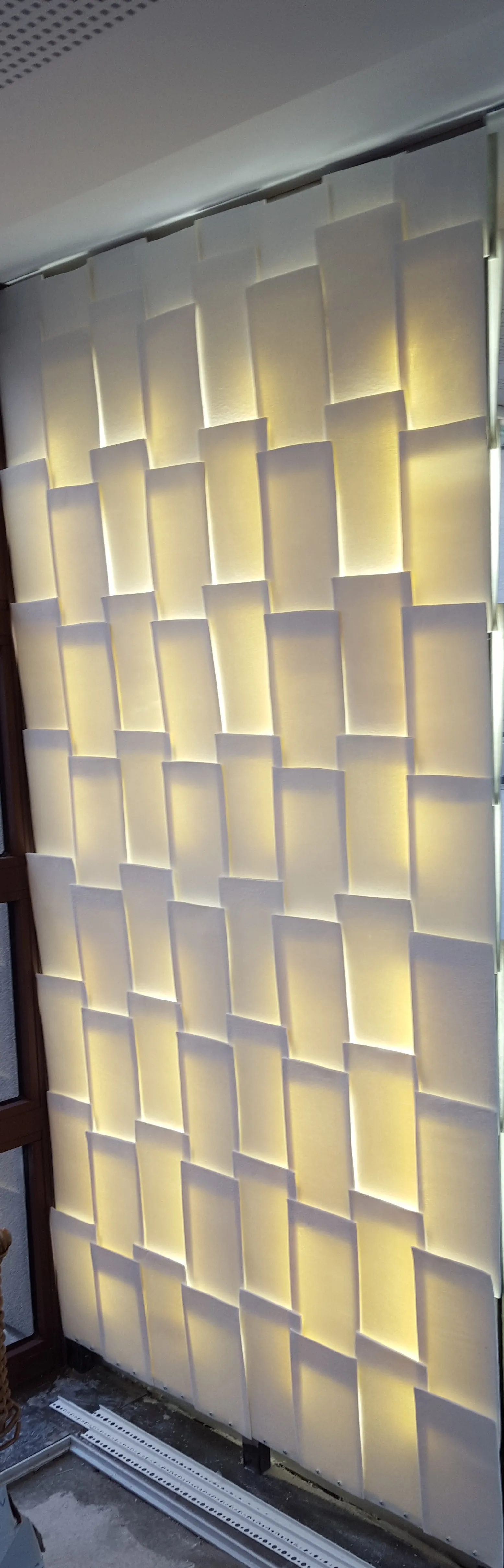Chantier : un mur de lumière en cours de pose, ses plaques de porcelaine déjà allumées du sol au plafond, dans un local encore brut.